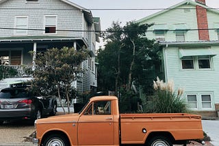 color photo of two houses with an older orange pickup truck parked out front