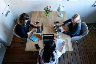 3 women with laptops sitting around a table