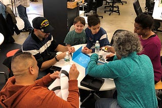 Veterans and families seated around a table, opening robot kits at our Battle of the Bots event in January 2019
