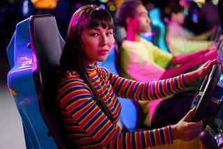 A woman in a colorfully-striped sweater plays a racing game at an arcade