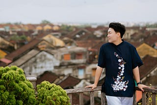 A man leaving on a wooden railing while looking at the view of a town.