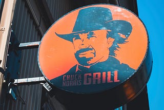 An orange sign featuring Chuck Norris in a cowboy hat. The sign reads, “Chuck Norris Grill.”