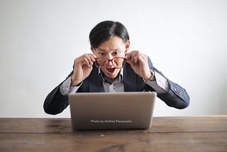 A formally dressed man surprised by what he is seeing on his laptop.