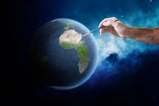 The image depicts a human hand holding a paintbrush, which is touching a realistically rendered Earth against the backdrop of space. The Earth is centered on the South American continent, which is illuminated by the brush as if being painted or highlighted by the artist. The surrounding space is deep blue and dotted with stars, giving the impression that the Earth is being artistically enhanced or created within the vast cosmos.