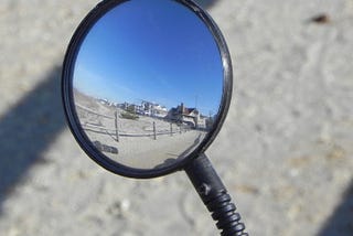 Looking into a bicycle mirror at some houses along the sandy shore