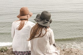 Decorative image: Two friends wearing sunhats sitting by the beach facing the water