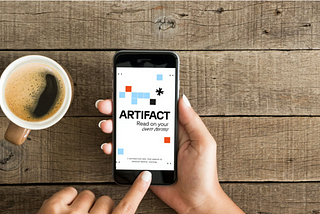 Picture of mobile app “artifact’ and a phone on a table next to a cup of cofee
