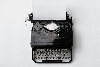 An antique typewriter with a sheet of paper sits on a white desk.