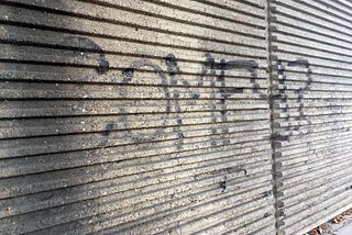 The word “Comfy” spray painted in black on grey corrugated concrete