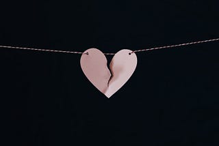 A paper shaped as a broken heart held up by a string that runs across the field of vision