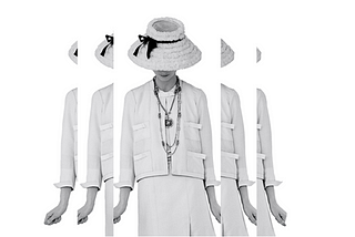 Black and white image shows Gabrielle Chanel wearing one of her signature suits, with her head down, from Gabrielle Chanel. Fashion Manifesto at the V&A Museum London. Soundscape by Coda to Coda.