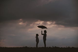 Silhouette of girl holding umbrella over another child