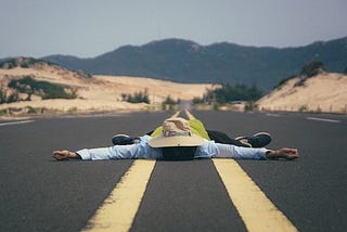 A man lies in the middle of a long desert highway.