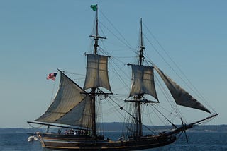 Photo of a two masted square-rigged brigantine under full sail, in front of blue sky and sailing on a darker blue sea.