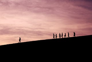 A group of 7 people walking downhill at sunset with one leader at sunset