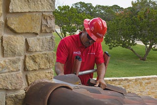 A Schulte Roofing professional on a ladder fixing a dark red and brown clay tile roof during the roof replacement process.