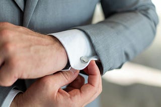 Man in grey suit adjusting cufflinks