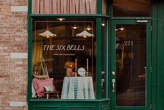 The front of The Six Bells stores, with a green door and large glass window showing a homewares display inside.