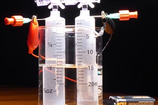 Simple electrolysis gear, with battery, wires, container of water, two plastic tubes.