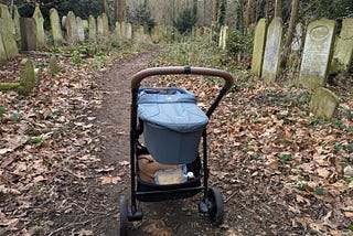 A pram on a path through headstones with trees behind them