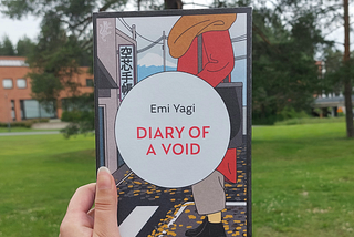 Fariza’s hand holding the copy of Diary of a Void with trees on grass and a building in the background