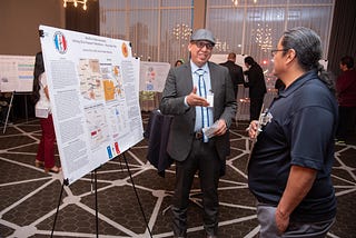 Javion Chee is at an ASU networking event sharing his poster presentation to an event goer.