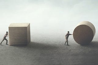 One man pushing a cube, another rolling a cylinder. The man with the cylinder is further ahead.