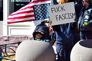 Protesters hold the U.S. flag upside down as a symbol of constitutional emergency, along with a sign that reads “Fuck Fascism”