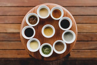 10 different colorful sauces arranged on a wooden serving dish resting on a wooden table.
