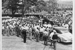 Black & white photograph of Fleet Admiral Chester W. Nimitz, Chief of Naval Operations, stands up in an open convertible. The Admiral is greeting or addressing a very large before the dedication of the Veterans’ Memorial in Steuben County Bath, New York, on 25 August 1946.