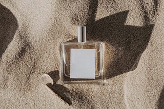 An empty, glass bottle of perfume sitting in beach sand.