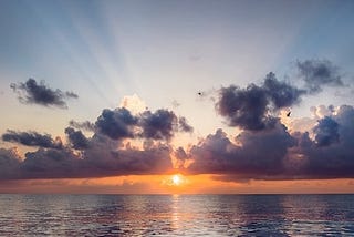 The start of a new day. Sunrise at sea, with rays of light beaming through the clouds, that gives us hope and inspires us into action.