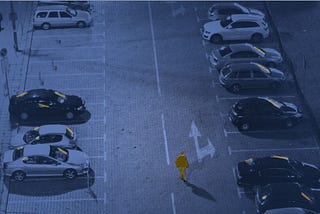 A single highlighted figure walks alone through a field of cars at night