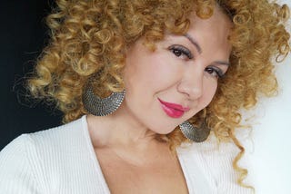 curly woman with big hoop earrings and low cleavage looking at the camera