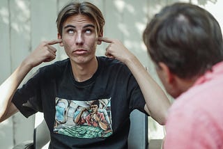 A teenager rolling his eyes and covering his ears while someone else is talking with him.