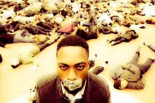 A Black Lives Matter protest with protestors laying as dead bodies on the ground with a Black Male with mask mouth covering.