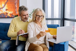 Elderly man and woman using a laptop and holding a credit card.