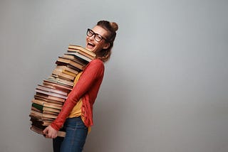 Happy woman carrying a giant stack of books.