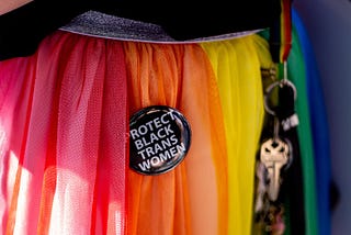 Close up of the rainbow skirt of a Gay Pride participant. A pin on the skirt reads “Protect Black Trans Women.”