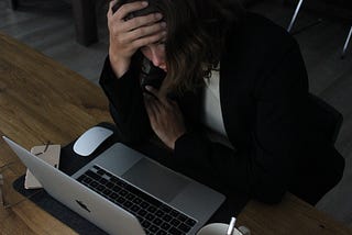 Woman leaning over laptop with her head in her hand, looking sad and tired.