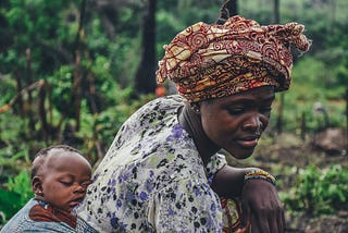 African woman working on a farm while carrying a baby on her back