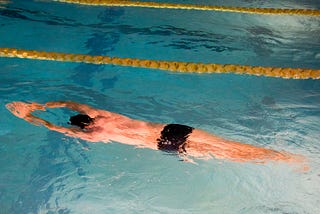A male swimmer in a swimming pool, stretched out with arms forward floating next to a yellow lane rope