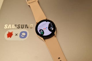 A Samsung Galaxy Watch4 placed on top of a Samsung Laptop. The watch shows the Samsung homepage on it’s face.