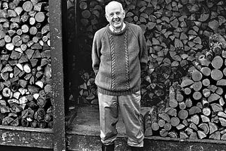 Farmer-philosopher Wendell Berry standing by a pile of chopped wood.