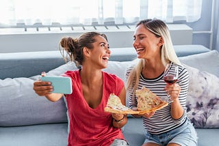 Two women eating pizza and drinking wine.