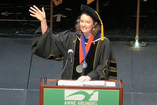 Dr. Hill waves at the crowd from a podium that says Anne Arundel Community College.