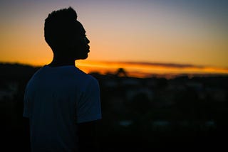 A sillouette of a man standing in front a sunset in a white shirt