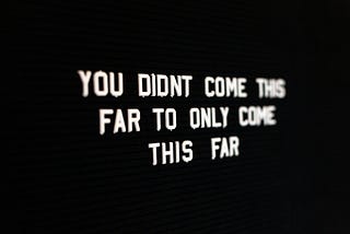 Stark white letters boldly contrast with a black background, stating, “You didn’t come this far to only come this far.” The text is clear and close to the reader on the left, and becomes blurry as it gets further away to the right.