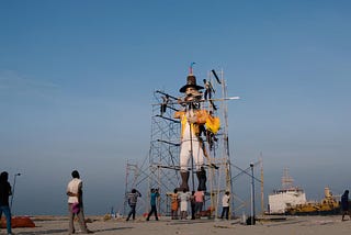A group of people are mounting a huge effigy with ropes and scaffolding with a blue sky in the background.