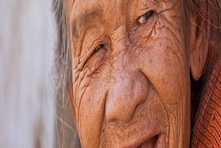 Elderly lady in an orange sweater smiling like a jokster.